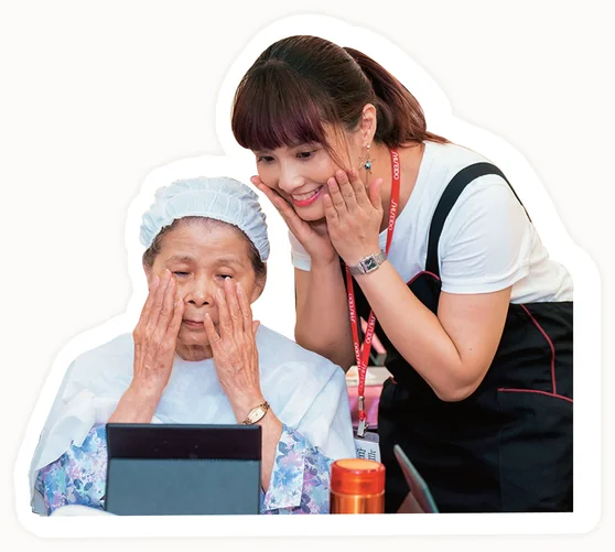 An older woman receiving a cosmetic therapy session, having her face gently touched by a caregiver